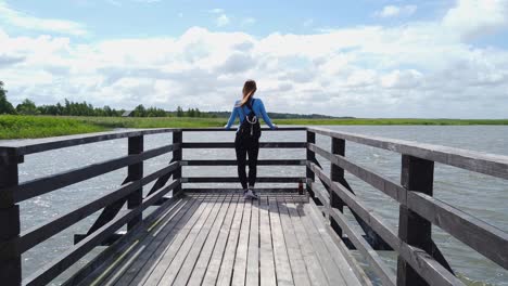 young woman standing on wooden pier, admiring breathtaking view of lake and natural landscape in poland