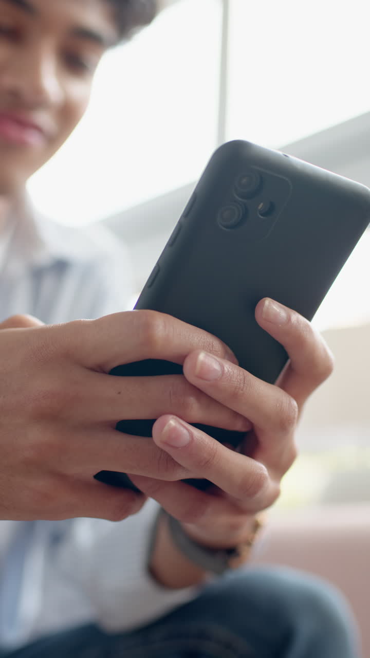 Vertical video: Person smiling while using smartphone at home, enjoying relaxed moment
