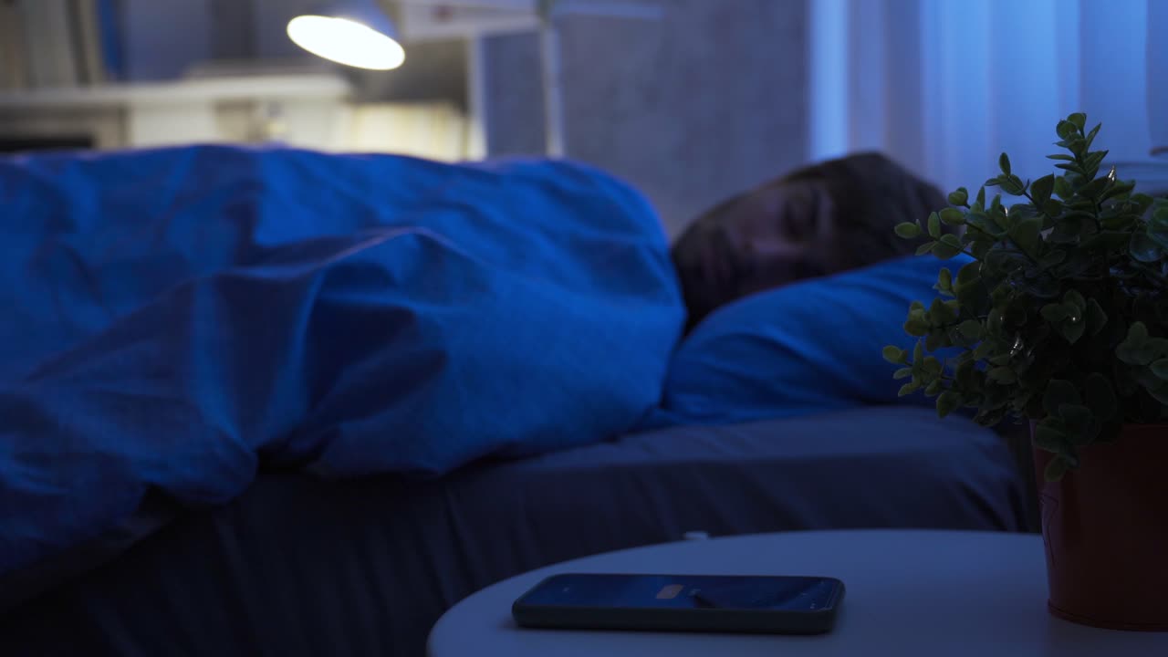 집에서 침대에서 자고 있는 젊은이가 알람을 해제하기 위해 깨어납니다.