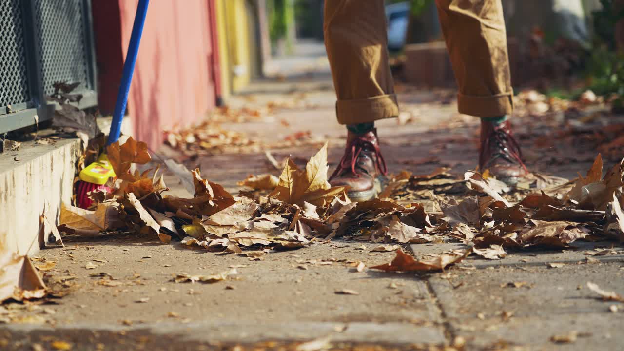 Person Sweeping Dry Autumn Leaves from a Sidewalk