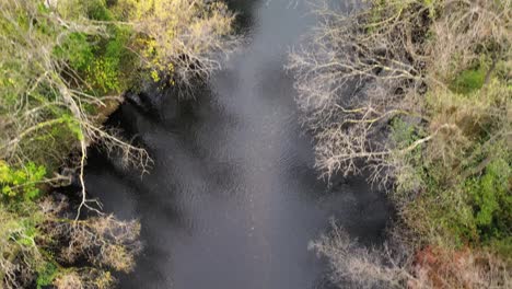 Flying-upward-shot-of-the-Rur-river-in-Kreuzau,-Germany-during-a-cold-Autumn-afternoon-next-to-a-pathway-and-farm-fields-with-a-view-of-a-small-walkover-bridge