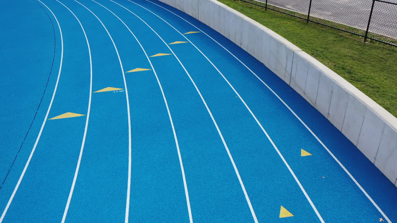 una plataforma rodante de ángulo bajo, filmada sobre una pista de atletismo azul