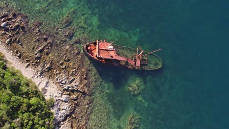 Altes-Kaputtes-Schiff,-Halb-Gesunken-Am-Seichten-Blauen-Wasserufer,-Von-Oben-Nach-Unten