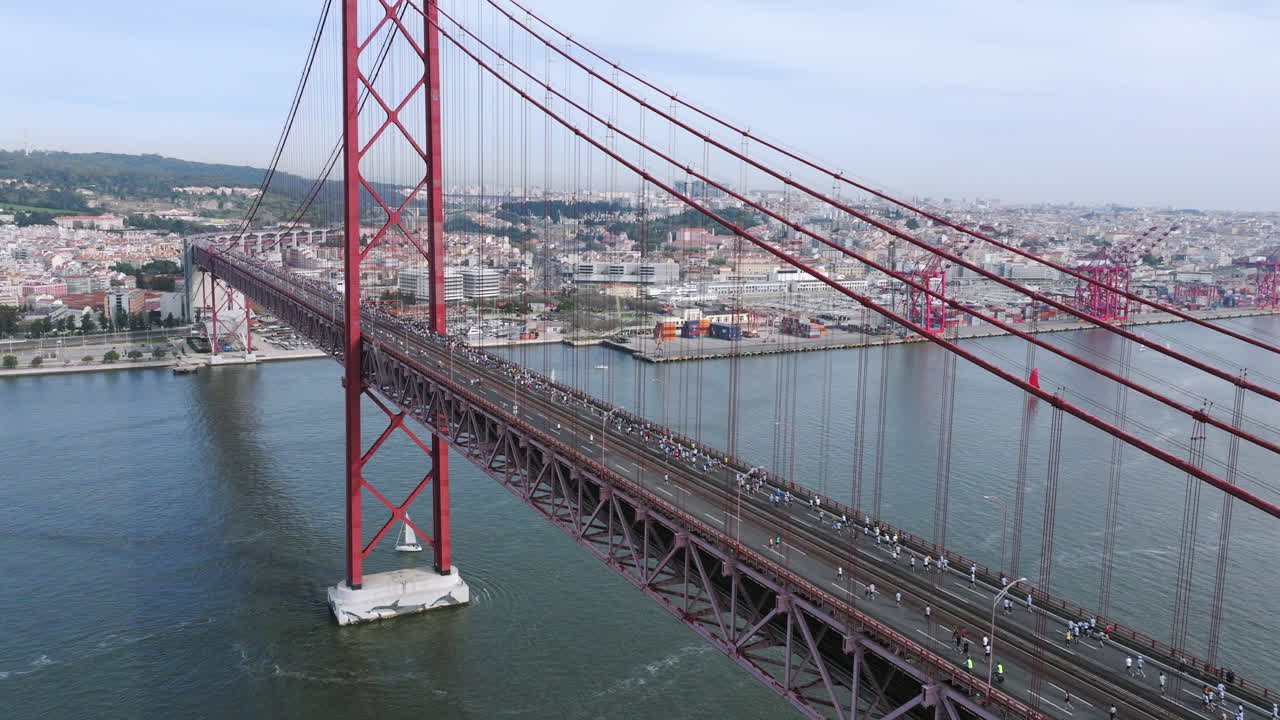 Half marathon and 10K long distance running event in Lisbon, Portugal, Europe. Runners crossing the iconic famous red 25th April suspension bridge. Professional panning drone aerial, neutral grading