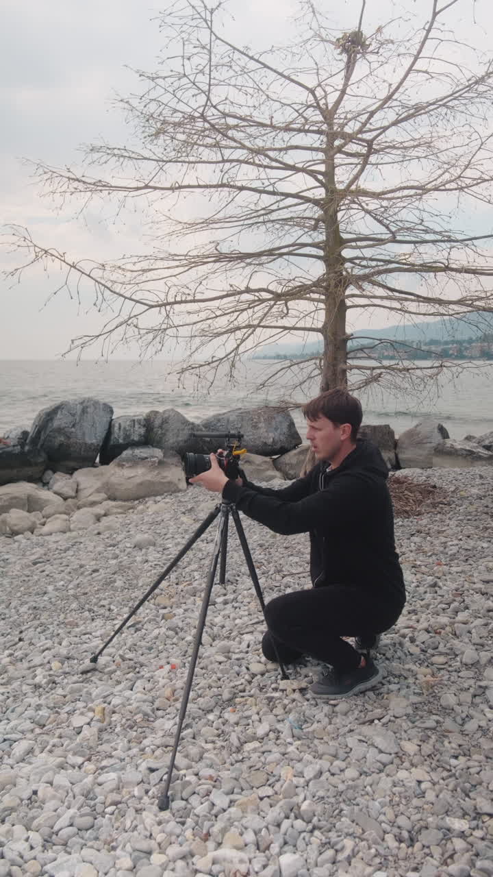 Vertikal: fotograf sætter et stativ op ved siden af en sø om dagen på en strand, statisk optagelse.