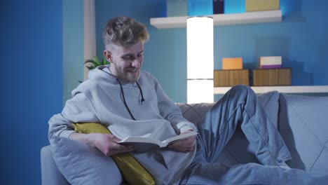 un joven feliz y guapo leyendo un libro pacíficamente en casa solo.