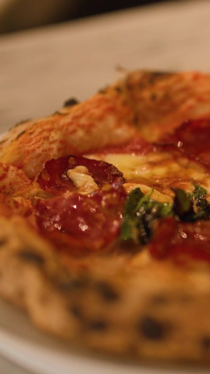 Primo piano di una mano che ruota una pizza al lievito madre con salame piccante su un tavolo di marmo.