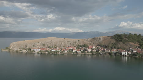 droneshot from above lin albania flying backwards on a cloudy day with the sun coming through the clouds with land and water underneath log