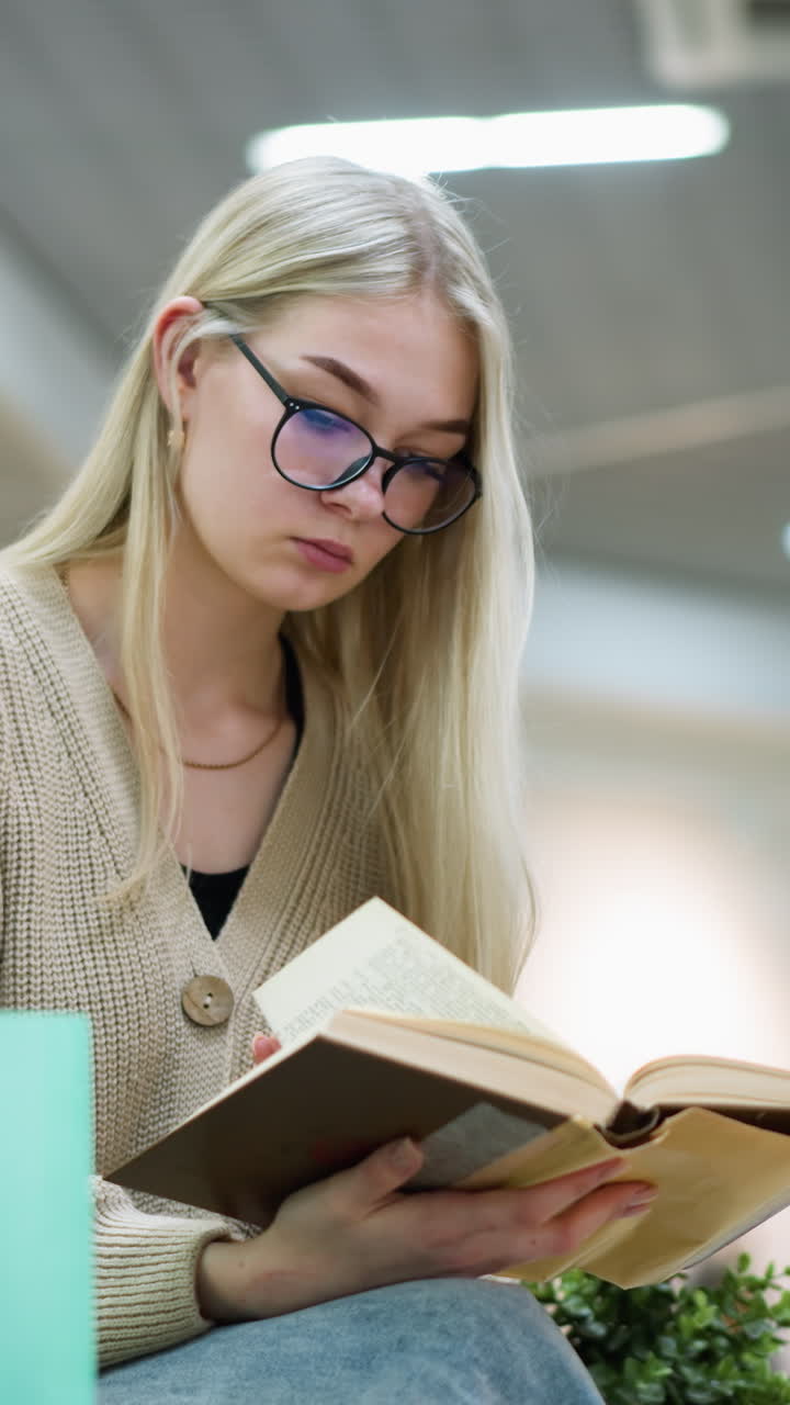una joven pasa reflexivamente por un libro con una bolsa de compras verde menta a su lado en un centro comercial bien iluminado, fondo ligeramente borroso, momento tranquilo