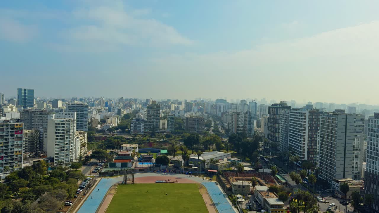 Overhead establishing pan of city buildings with sunset glow casting across rooftops and trees, Lima Peru