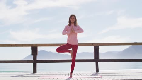 healthy mixed race woman practicing yoga outdoors, standing and stretching by the sea