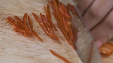 cortar un chile rojo picante en rodajas finas en una tabla de cortar de madera - cerrar