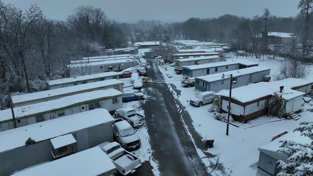 Comunidad de viviendas de bajos ingresos estadounidense cubierta de nieve en invierno. Casas móviles y coches aparcados bordean las calles heladas. Ambiente suburbano tranquilo y frío en Pensilvania. Toma aérea panorámica.