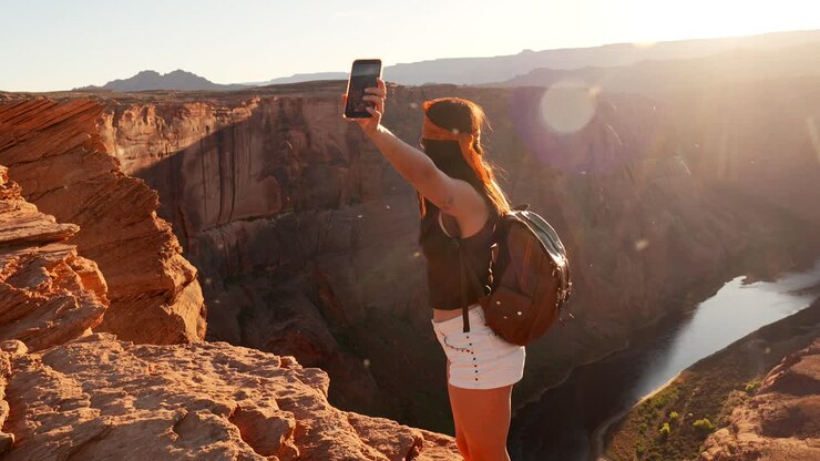Mujer joven tomándose una selfie con un smartphone en un mirador panorámico de cañón