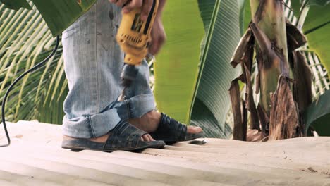 trabajador de la construcción que usa una herramienta de perforación para atornillar una hoja de zinc en una correa de ca que es parte de una estructura metálica en un sitio de construcción rural