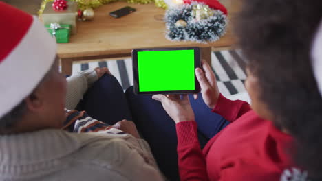 smiling african american mother with daughter making tablet christmas video call, with green screen