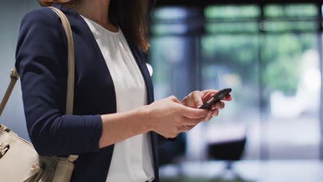 caucasian businesswoman with brown hair using smartphone in modern office