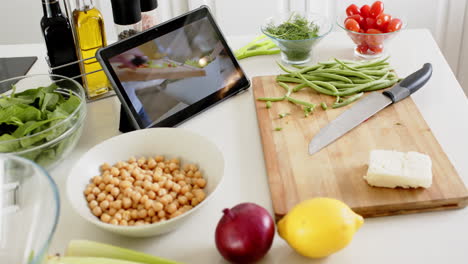 cuchillo, tabla de cortar, verduras y tableta en el mostrador en la cocina soleada, cámara lenta