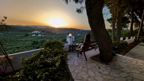 Revealing-shot-Caucasian-young-brunette-woman's-back,-staring-at-sunset-sitting