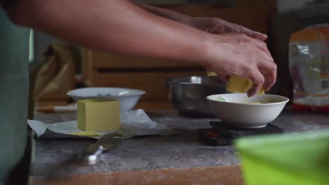 Cubes-of-cut-butter-placed-into-bowl-and-measured-on-ingredient-scale,-filmed-as-medium-closeup-slow-motion-handheld-shot