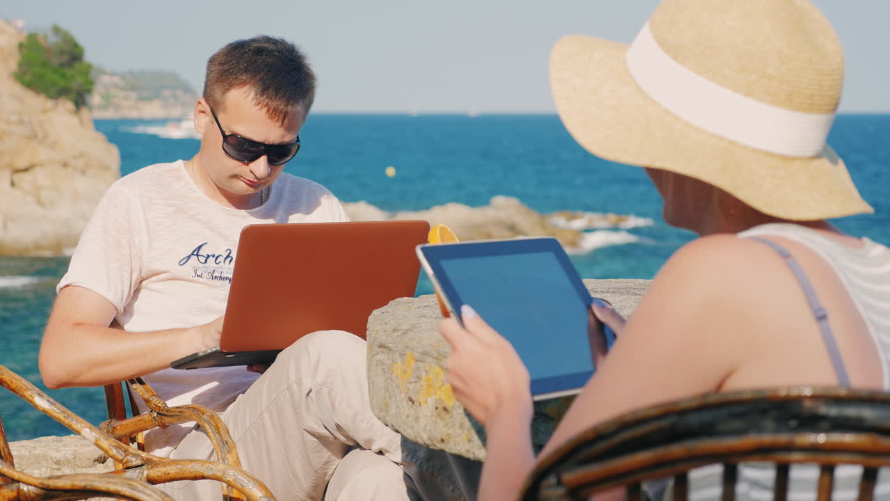 молодая пара на отдыхе мужчина использует ноутбук женщина с планшетом с видом на море