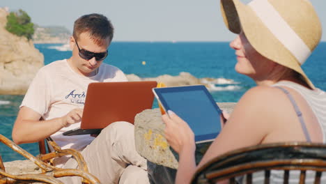 a young couple on vacation a man uses a laptop woman with a tablet with sea views