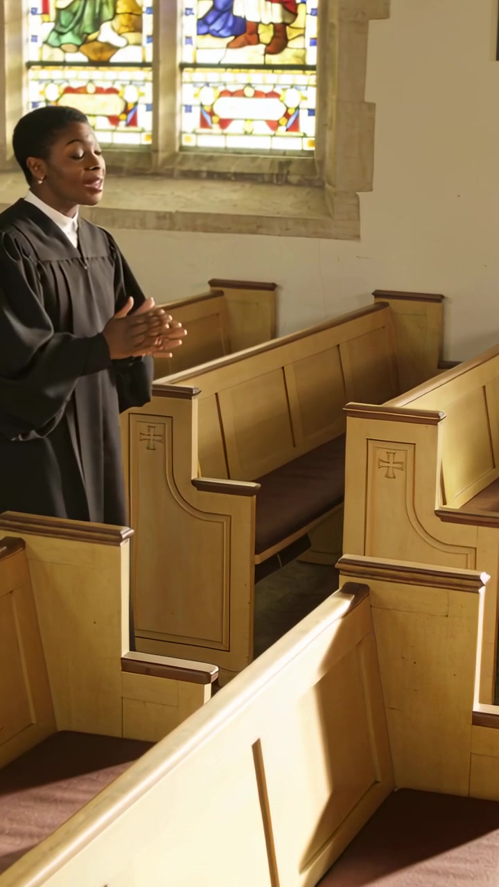 Video verticale: Donna che applaude in abito da coro, canta lodi, banchi della chiesa, vetrate colorate, spazio per il testo.