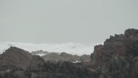 Waves-crashing-on-beach-with-rocks-in-foreground