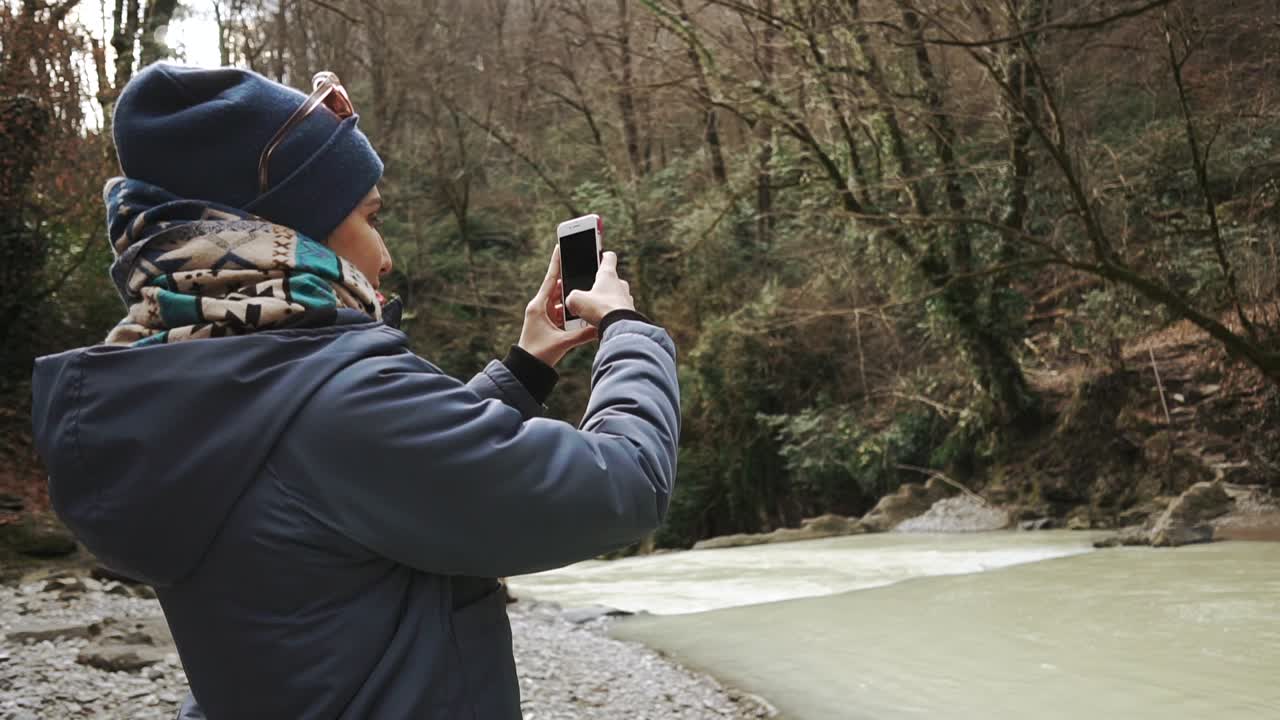 Woman taking a photo of a river in a forest