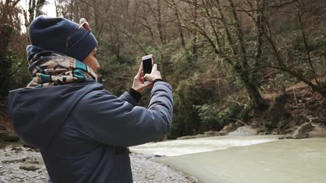 woman taking a photo of a river in a forest