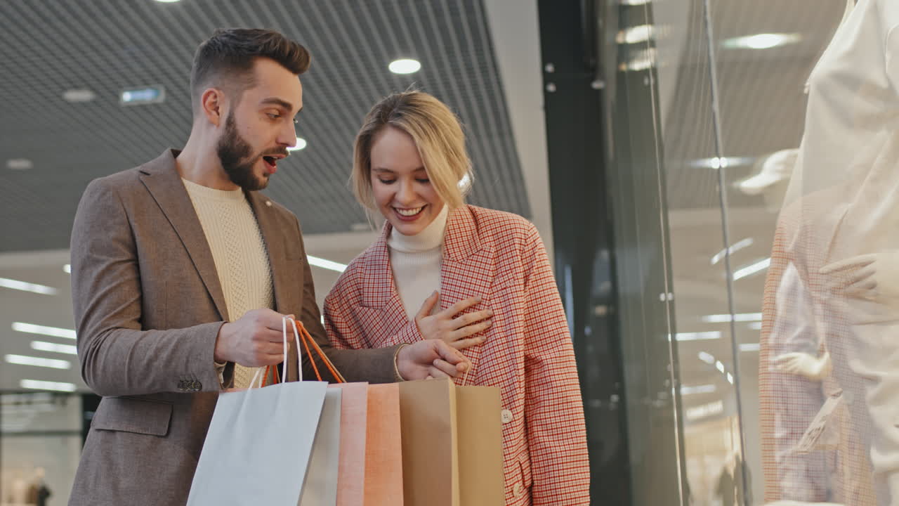 Man Showing Purchases In Shopping Bags To Girlfriend