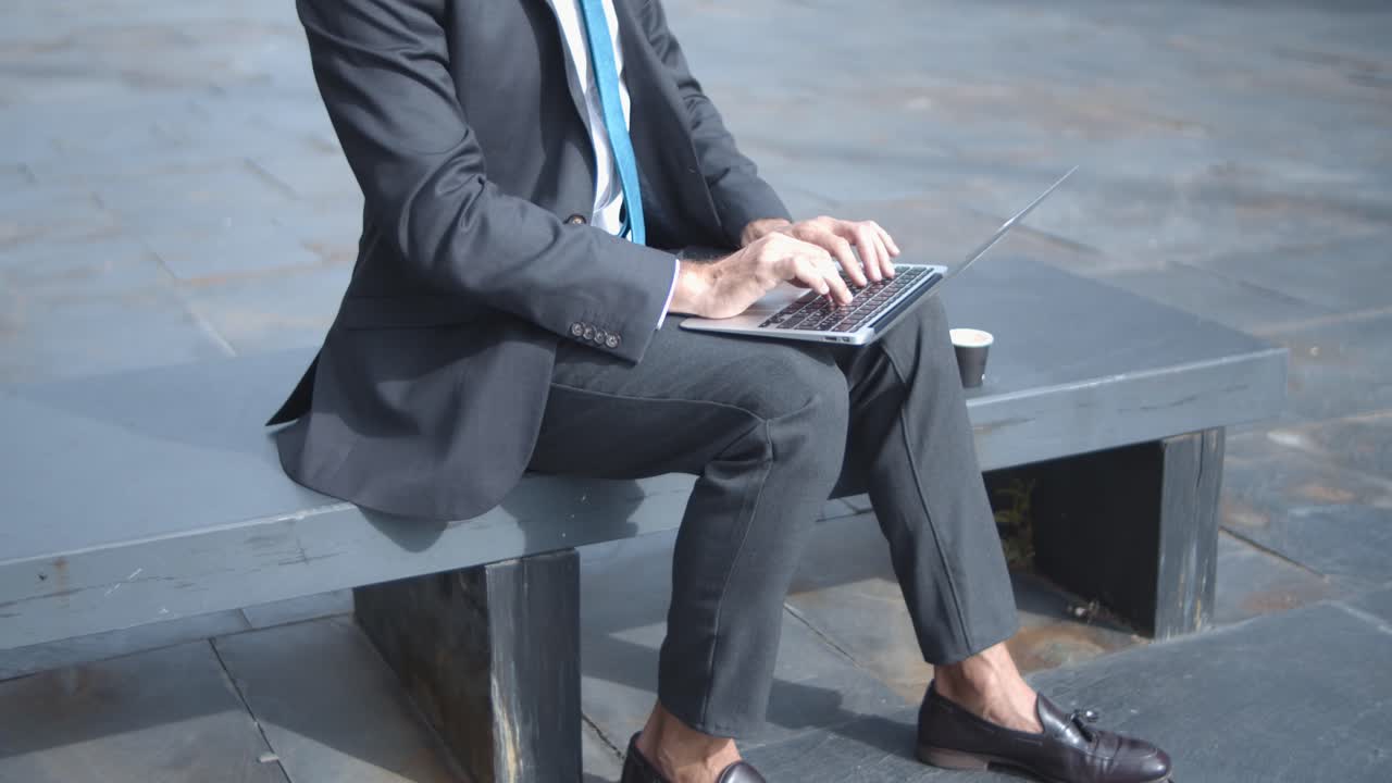 테이크 아웃 커피 컵과 함께 벤치에 앉아있는 동안 노트북에 입력하는 집중된 대머리 사업가