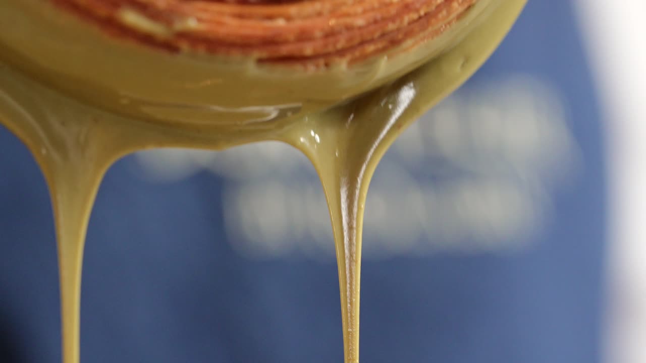 Pistachio croissant donut being decorated cream dripping close up