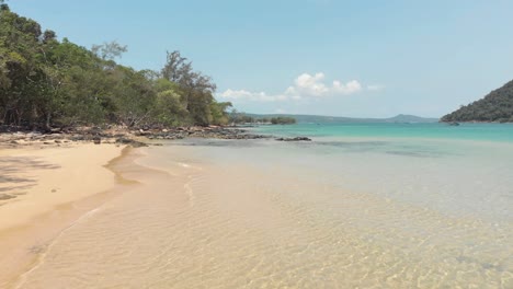 clean shallow water washing coast and sweeping the exotic shore in m'pai bay, koh rong sanloem, cambodia - aerial ground level fly-over shot