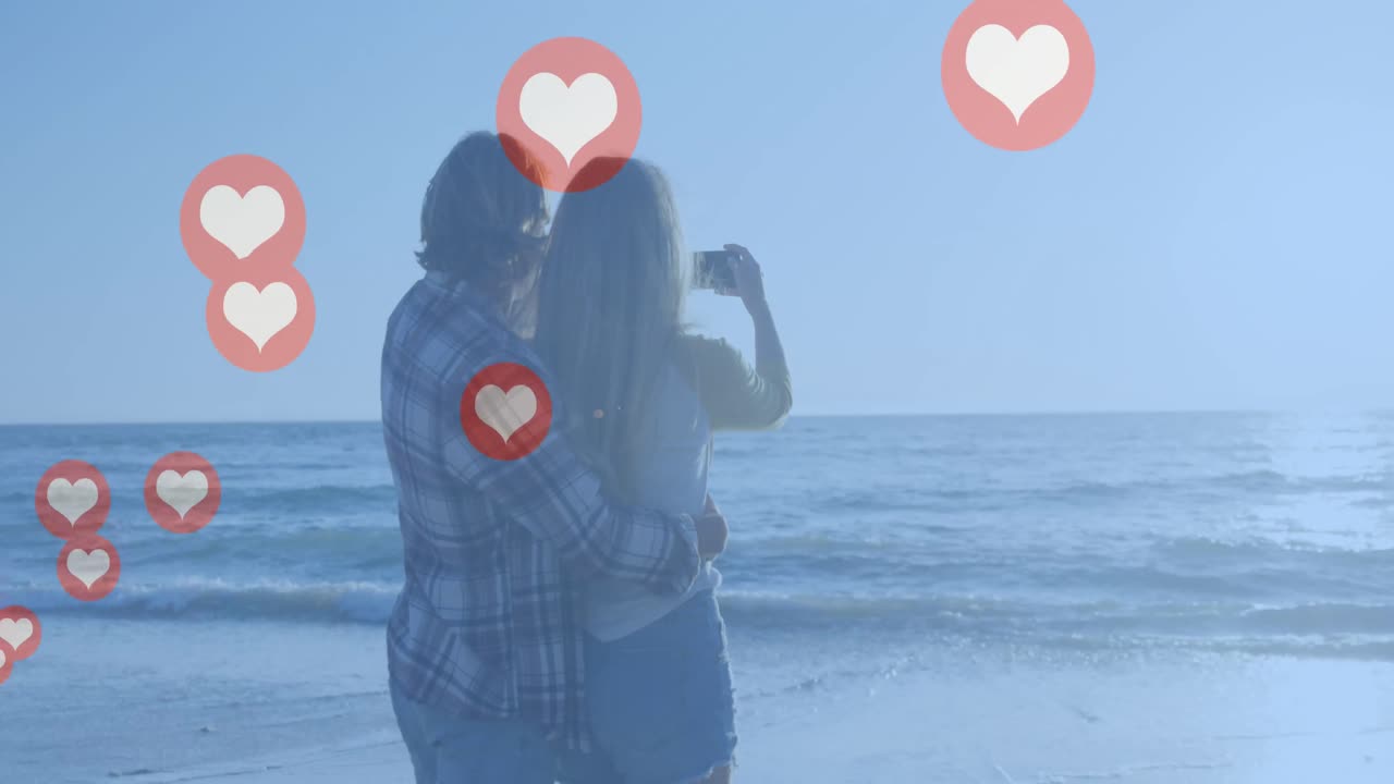 해변에서 사진을 찍는 백인 부부 에 대해 떠다니는 여러 개의  ⁇ 은 심장 아이콘
