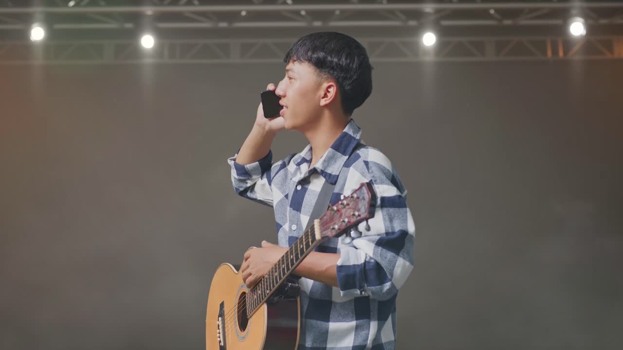 무대에 서서 스마트폰으로 대화하는 기타를 들고 있는 아시아 십대