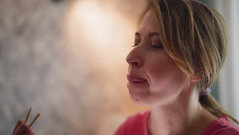 close up of lady in pink top eating happily and licking chopstick after savoring meal while seated in cozy indoor setting with soft blurred background