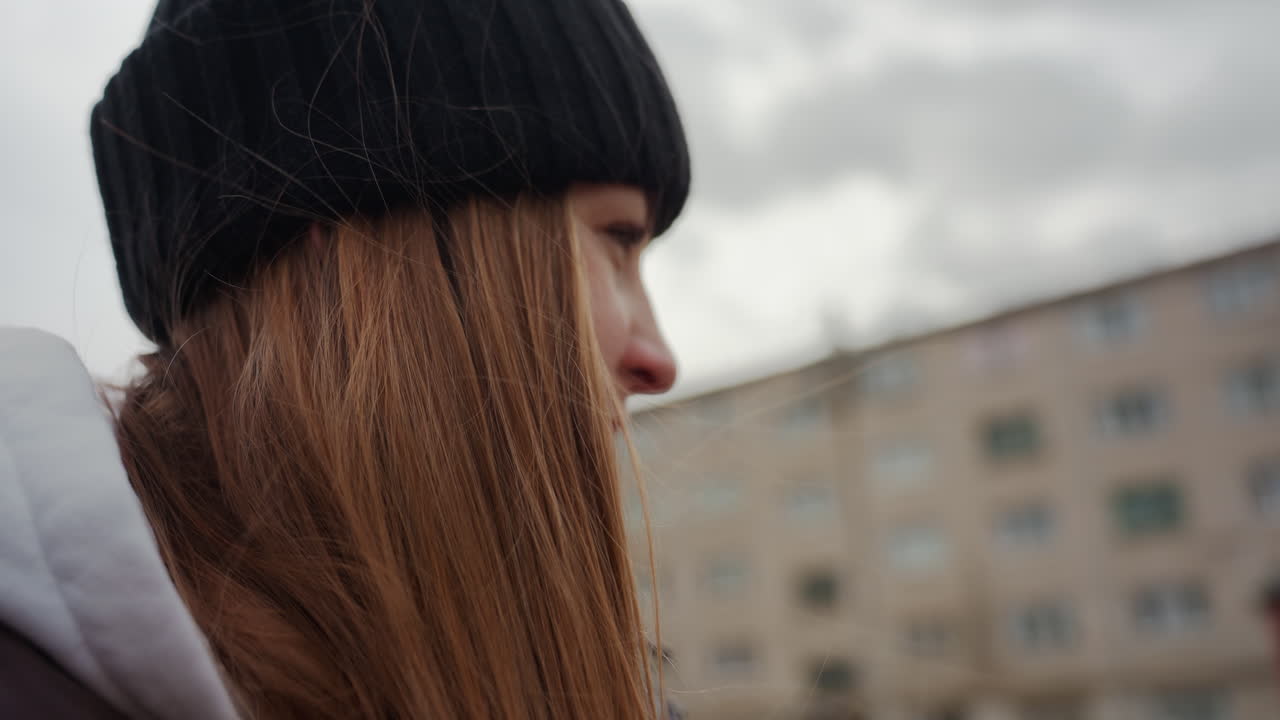 serena contemplación urbana, figura femenina serena con accesorios suaves en un entorno urbano al aire libre, mujer tranquila con cabello peinado y expresión amable de pie en medio de un fondo de apartamentos