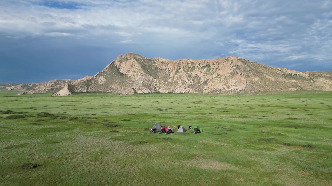 Rekaman udara menjauh dari tenda-tenda perkemahan sepeda motor di padang rumput Mongolia yang hijau