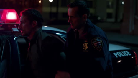 police officer apprehending a man by a patrol car at night