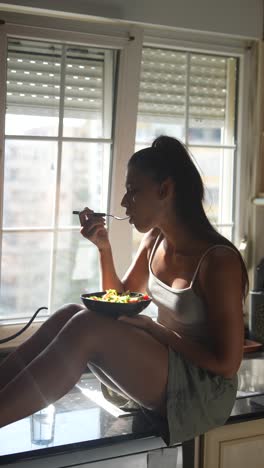 mujer comiendo ensalada junto a la ventana