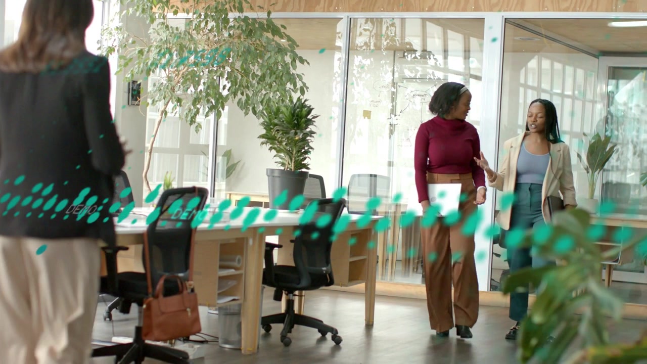 Two women starting business chat, walking to desks holding laptop, teal overlay obscuring subjects