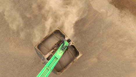 a close-up aerial view of an excavator's scoop filling with sand, highlighting the texture and movement