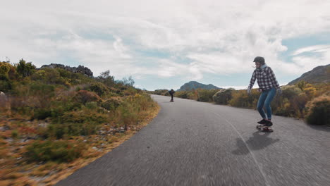 Junge-Multiethnische-Freunde-Fahren-Gemeinsam-Schnell-Auf-Einer-Wunderschönen-Landstraße-Longboarden-Und-Genießen-Extremsport,-Indem-Sie-Bergab-Fahren-Und-Tricks-In-Zeitlupe-Machen