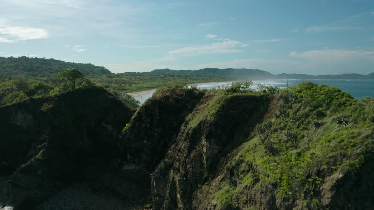 Tampilan Drone Tanjung Pesisir dengan Longsor Kecil dan Erosi yang Terlihat, di Mana Ombak Menghantam Tebing, Menyingkap Garis Pantai Hijau Subur yang Membentang Jauh