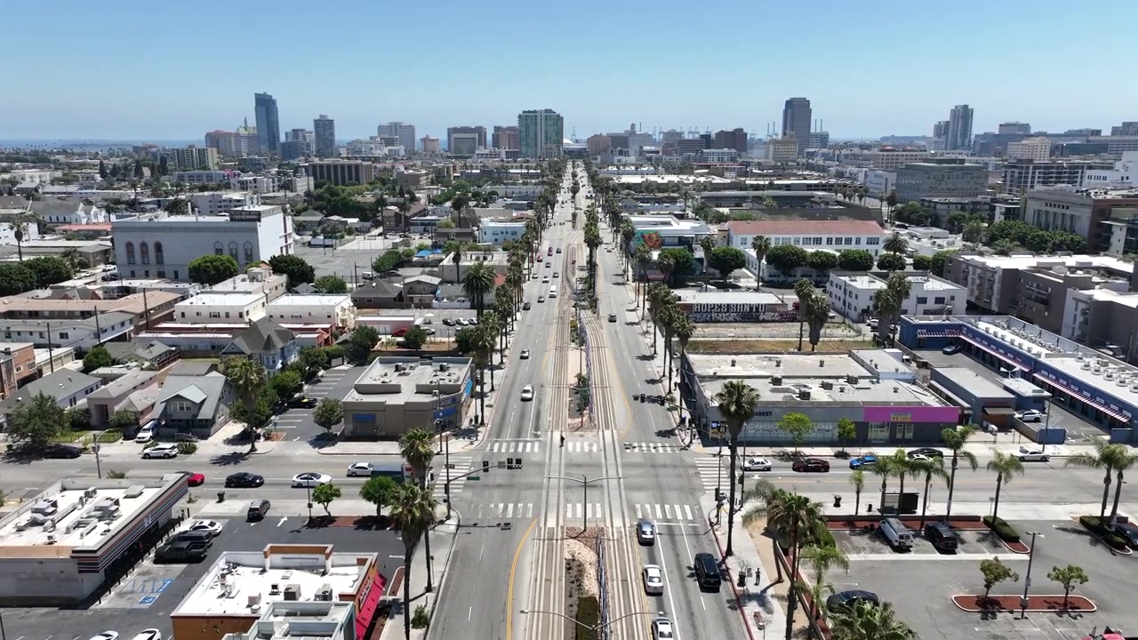 Filmato aereo cinematografico con drone di East Long Beach Boulevard a Long Beach, California, USA, che mostra traffico in movimento, quartieri urbani, linee ferroviarie, edifici commerciali e lo skyline del centro di Long Beach.