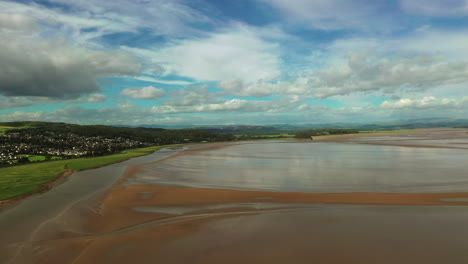 Aerial-away-motion-shot-of-a-coastal-bay-at-low-tide-with-the-shallow-water-shinning-in-the-sunlight