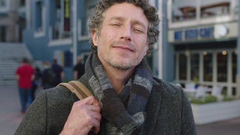 slow motion portrait of attractive mature caucasian man enjoying travel lifestyle smiling at camera in urban city wearing scarf