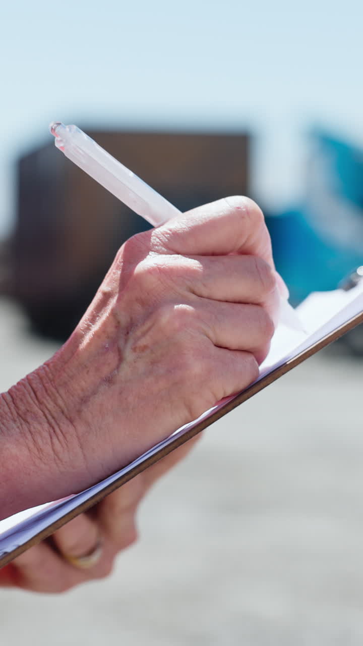 Primer plano de una mano escribiendo en un portapapeles al aire libre.