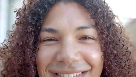 portrait close up of eyes of happy biracial man with curly hair smiling in sunny garden, slow motion